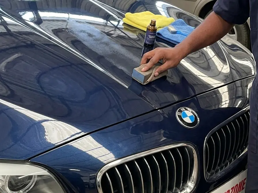 Ceramic coating being applied by hand to a blue BMW's bonnet