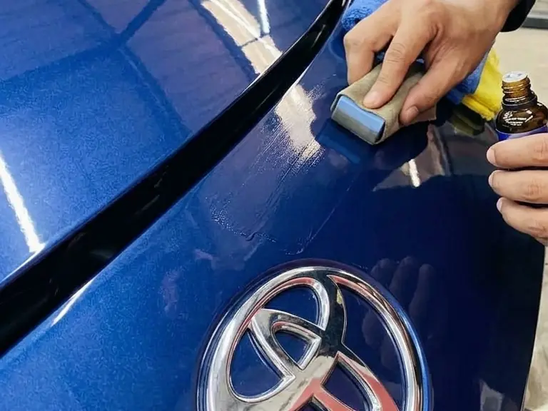 Ceramic coating being wiped onto a blue car's bonnet