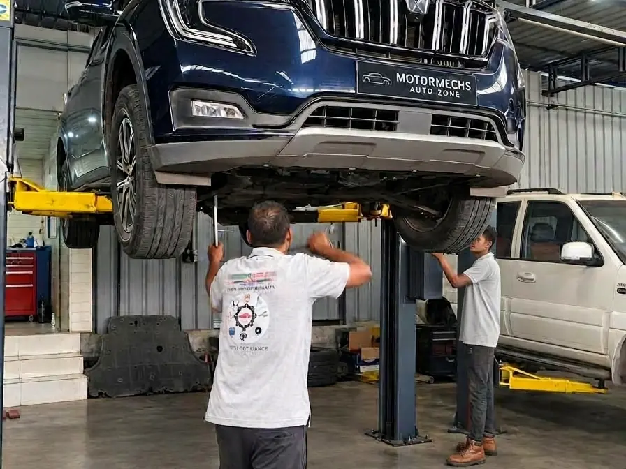 Mahindra XUV700 raised on a lift with mechanics working underneath