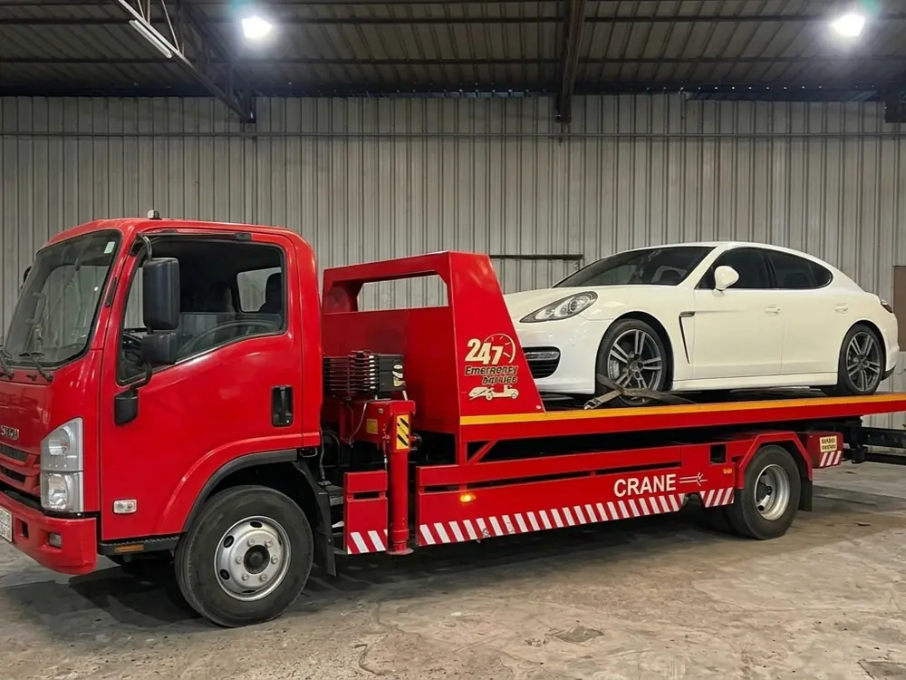 Red flatbed recovery truck carrying a white Porsche Panamera