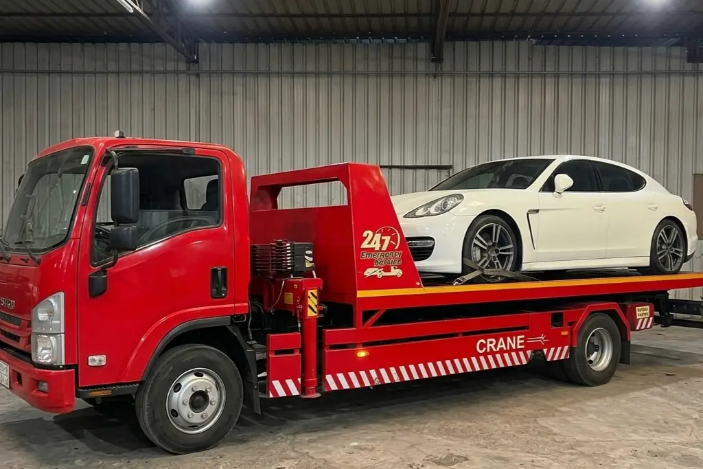 Red flatbed recovery truck carrying a white Porsche Panamera